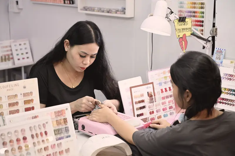 Salón de uñas con muestrarios de color y una manicurista atendiendo (foto ilustrativa)